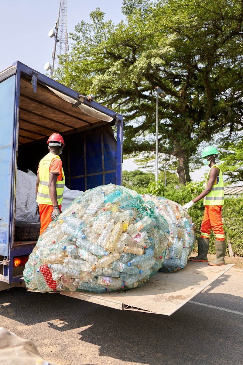 Two workers in protective gear loading plastic bottles onto a truck outdoors.